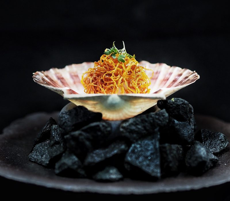 Nordic scallop dish with crispy garnish, elegantly served in a shell over volcanic stones – an exclusive seafood creation for luxury yacht catering in Monaco.